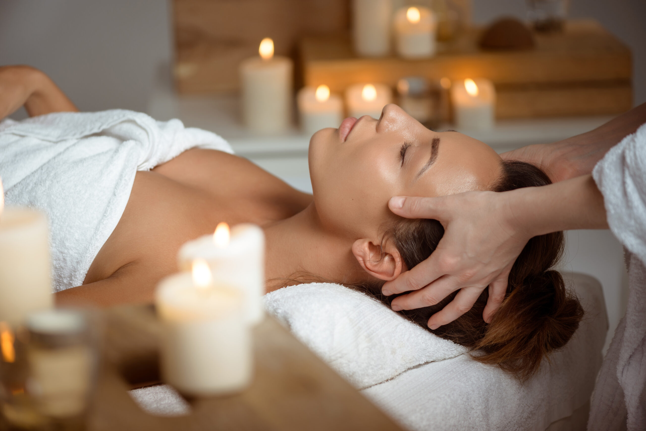 Young beautiful brunette girl having face massage relaxing in spa salon. Eyes closed. Copy space.